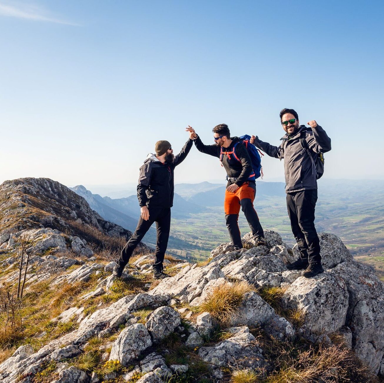 About Finance Now webpage hero image - A group of three cheerful hikers standing on the summit of a mountain