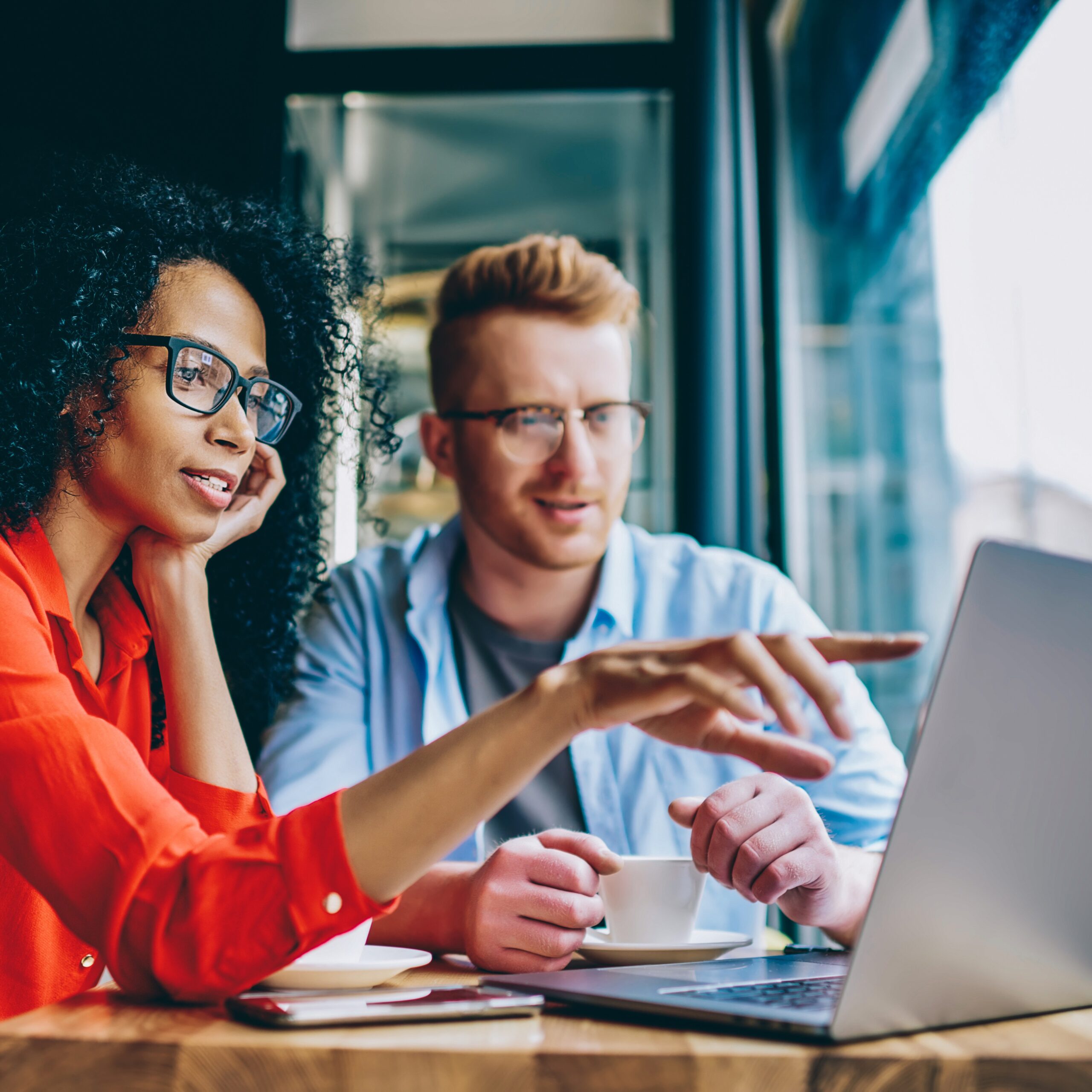 Female graphic designer pointing with finger on laptop computer during collaboration with colleague on common project in coffee shop.